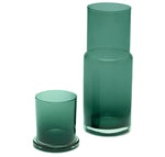 The Pigeon & Poodle Faro Smokey Green Carafe and matching tumbler feature hand-blown glass with cylindrical shapes and clear bases, exemplifying refined hospitality against a white background.