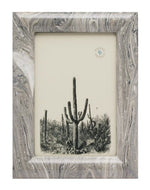The Gray Swirled Ashland Frame by Pigeon & Poodle, sized 4 x 6, features hand-painted lacquered resin with a marbled gray finish and displays a black-and-white illustration of tall cacti in a desert landscape.