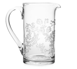 The Berry Ascutney Pitcher by Simon Pearce is crafted from lead-free glass, featuring a curved handle and an etched floral pattern inspired by wild berry brambles around the middle and lower half.