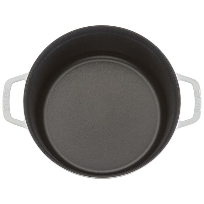 Top view of an empty round black Staub Cast Iron Dutch Oven Collection piece with two white handles, ideal for slow-cooking, on a white background.