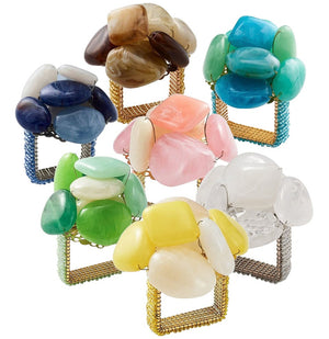 A set of six Kim Seybert Sea Stone Napkin Rings, featuring large, colorful polished stones and gold or silver mesh bands, are grouped together on a white background.
