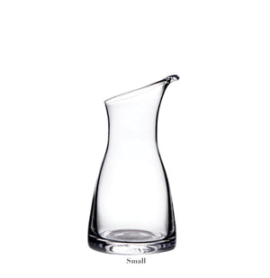 The Simon Pearce Barre Carafe Collection features a handmade glass carafe with a narrow base, wide middle, and slanted opening. Shown upright on a white background with "Small" labeled below.