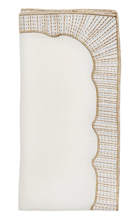 The Kim Seybert Frame Napkin Set features folded white linen napkins with gold and silver stitching on one scalloped and one straight edge for subtle metallic accents.