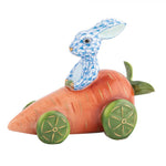 The Herend Carrot Car Bunny, Blue, is a charming porcelain rabbit with hand-painted designs, riding on a carrot-shaped car with vibrant green wheels.