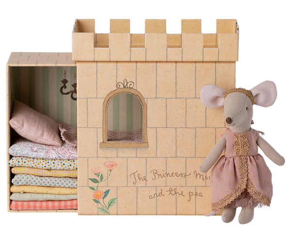 A Maileg Princess and the Pea Mouse dressed as a princess standing beside a cardboard castle playset with a stack of patterned mattresses inside, inspired by the fairy tale "The Princess and the Pea.