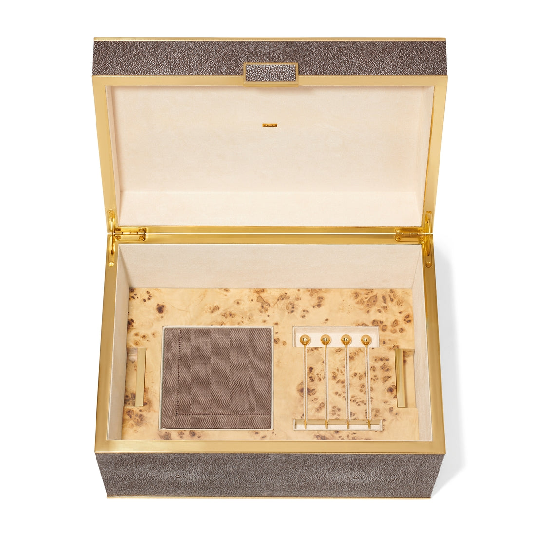 The Aerin Chocolate Classic Shagreen Bar Set features an open shagreen box with gold trim, a folded cloth, and four gold and glass cocktail picks on a beige, wood-patterned interior—an elegant home bar accessory.