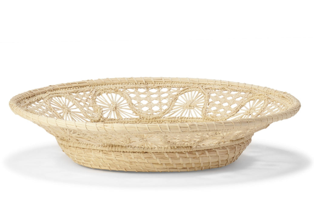 The Large Raffia Basket by Aerin is a shallow, oval basket handcrafted by Colombian artisans from light-colored natural fibers, featuring an open lattice design around the sides.