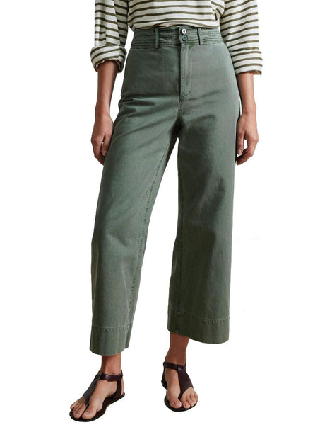 A person wearing the Apiece Apart Merida Pant, a high-waisted, wide-legged pant in green, and a striped shirt paired with black sandals.