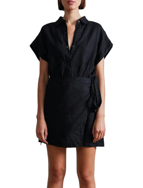A woman in an Apiece Apart Catania Wrap Mini Dress with dolman sleeves and a self-tie waist, standing against a white background.