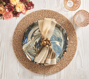 A table setting featuring the Kim Seybert Emberfall Placemat, a marbled plate, beige and tan napkin with a decorative ring, clear glassware, and a floral bouquet.