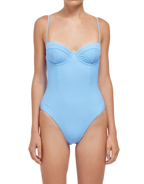 A woman posing in a light blue Simkhai Chantae one-piece swimsuit, crafted from recycled nylon, with a bustier top design.