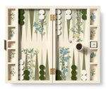 The AERIN x Gracie Heathcote Lacquer Backgammon Set by Aerin features a Heathcote design with green and white checkers, dice, a doubling cube on 16, and a cup, all set against a hand-painted wallpaper backdrop.