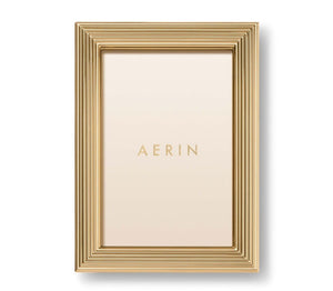 A gold rectangular photo holder from the Alessio Frame Collection by Aerin, this frame features a reeded design with layered ridges and displays a blank insert printed with "AERIN"—ideal for showcasing elegant photographs.