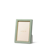 The Piero Leather Frame Collection by Aerin features a vertical green leather frame with gold accents and a gold inner border, displaying an "AERIN" placeholder card against a white background for an elegant touch.