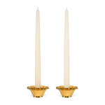 Two white taper candles stand in the Olivia Brass Taper Candleholder Set by Aerin, featuring elegant brass holders with a hint of Art Deco style, set against a plain white background.