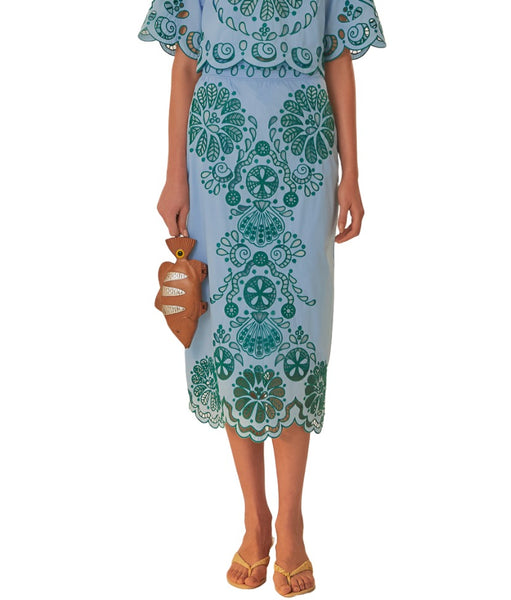 A woman wearing a Farm Rio Light Blue and Green Graphic Richelieu Skirt with yellow sandals, holding a small brown handbag.