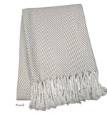 The Nantucket Herringbone Throw Collection by A Soft Idea in Sand features a beige and white cotton throw with hand-knotted fringe, folded neatly.