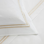 The Classic White/Khaki Bedding Collection by Frette features a luxurious 100% cotton sheet set with beige double-line borders and the brand name "Frette" embroidered on the pillowcase.