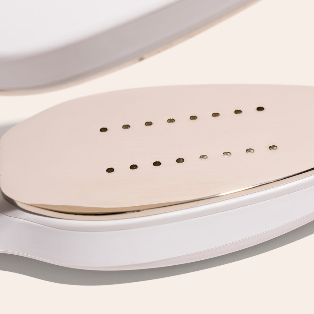 Close-up of a beige Nori Inc, Nori Press Steam Iron with a metal plate featuring many small holes, ideal for travelers seeking a compact solution.