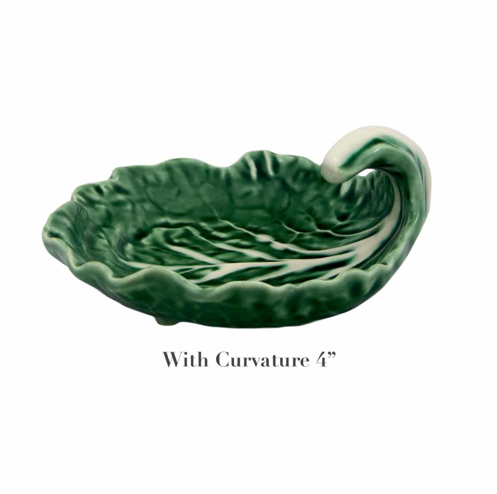 The Bordallo Pinheiro Cabbage Leaf Green Collection features a green ceramic dish designed like a leaf with a curled tip, evoking cabbage serveware. It reads "With Curvature 4" and showcases the artistry of Portuguese handmade craftsmanship.