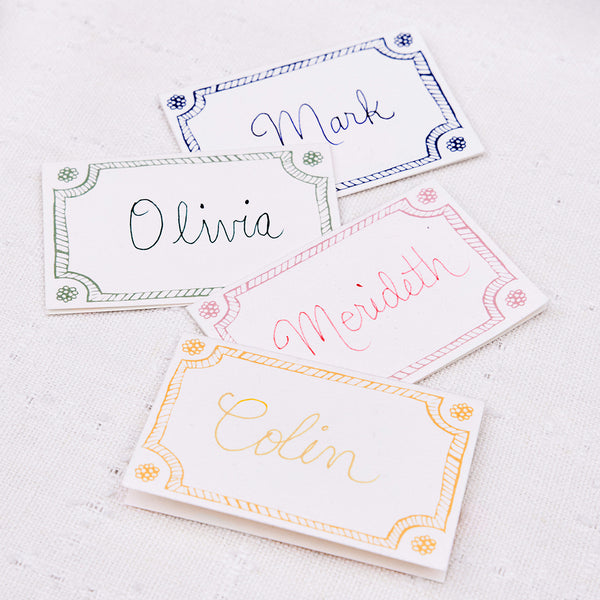 Four Berry & Thread Place Cards by Juliska, featuring decorative borders and labeled Mark, Olivia, Meridith, and Colin, are arranged on white fabric to showcase the timeless elegance of the collection’s classic motif.