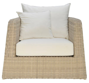 The Janus et Cie Zeya Outdoor Lounge Chair is a beige wicker armchair with weather-resistant white seat and back cushions, plus two square white pillows—ideal for outdoor living and shown from the front.