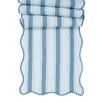 The Juliska Cabana Stripe Tabletop Collection features a folded fabric with blue and white cabana stripes, scalloped trim, and wavy edges.