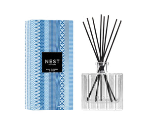 The Nest Blue Cypress & Snow Collection reed diffuser features a patterned glass bottle with black reeds and comes in a blue and white geometric box—ideal for adding a cozy winter scent to your space.