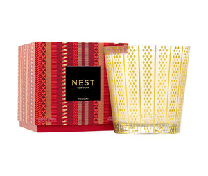 A Nest Holiday Collection candle in gold-patterned glass sits beside its red and gold box, filling the room with a festive scent.