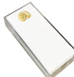 A clear Lucite holder displays a stack of Black Ink Nautilus Shell Skinny Notepads, each featuring a gold foil nautilus shell design in the top corner.