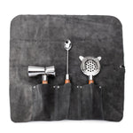 The Simon Pearce Acacia Bar Tool Set includes a gray suede roll-up pouch with separate pockets for a double-sided jigger, bar spoon, and julep strainer, each featuring wooden handles.