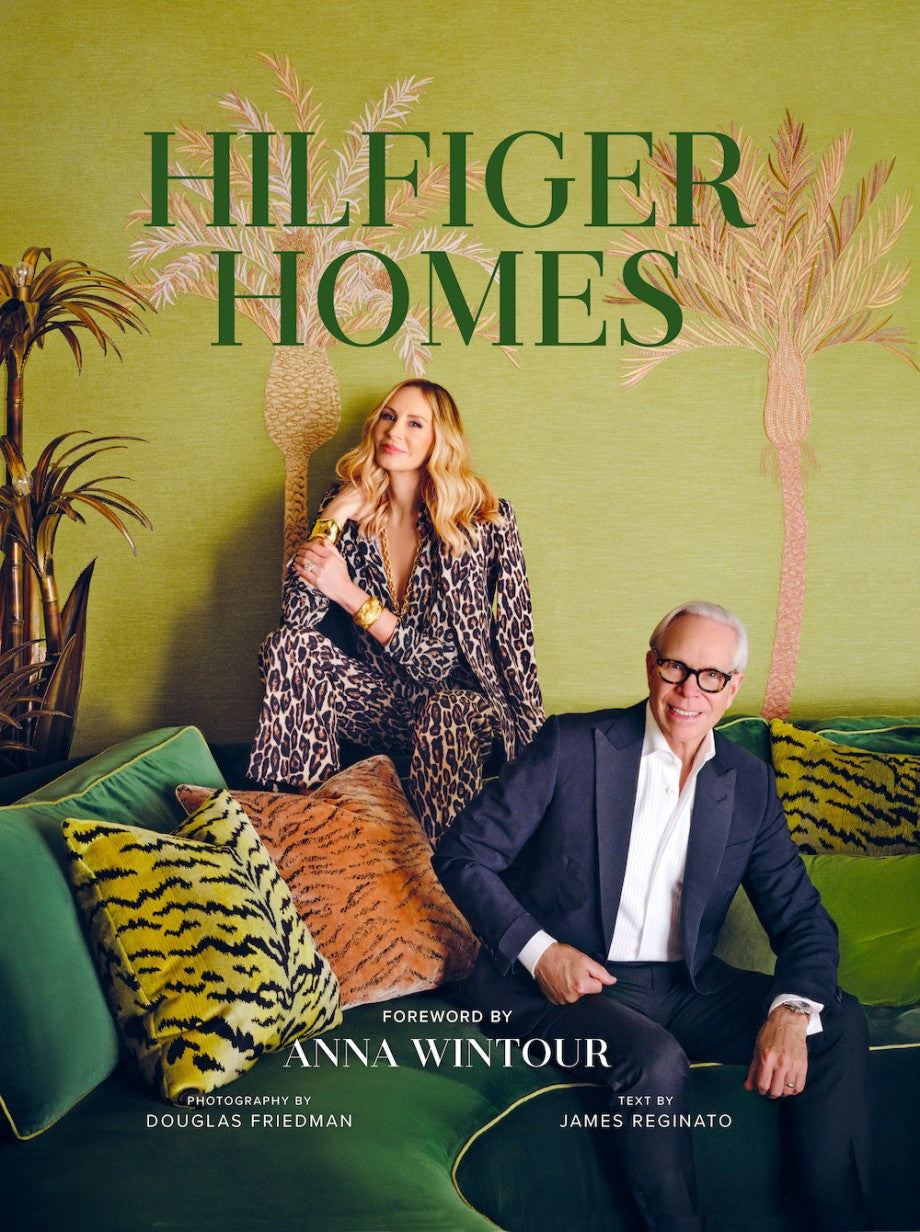 A woman in leopard print and a man in a suit sit on a green sofa with tiger-print pillows, highlighting Abrams’ Hilfiger Homes collection, with "Hilfiger Homes" displayed above.