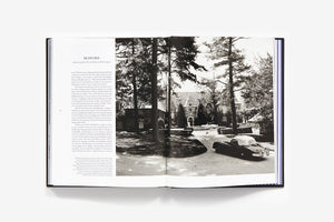 An open book, "Ralph Lauren: In His Own Fashion" by Abrams, shows a text page on the left and a black-and-white photo of a large house, circular driveway, and vintage convertible—ideal for any stylish coffee table.