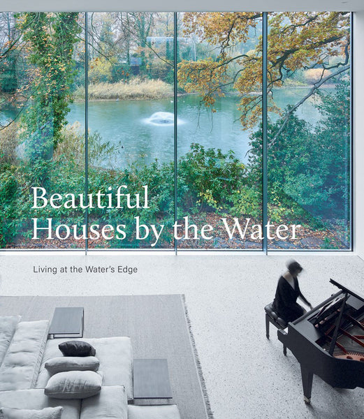 A person playing a grand piano in a contemporary home with large windows overlooking a tranquil waterfront setting, featuring Beautiful Houses By The Water by Common Ground.