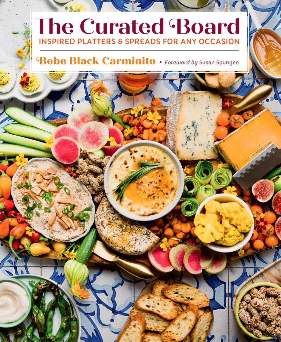 A vibrant array of cheeses, dips, veggies, fruits, bread, and crackers on a patterned board; cover of “The Curated Board: Inspired Platters & Spreads for Any Occasion” by Abrams—your guide to stunning themed boards and easy recipes.