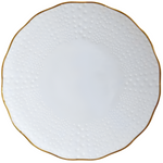 The Corail Gold Collection by Medard de Noblat/Devine features a white porcelain plate with a dotted, textured rim and thin gold trim on its scalloped edge, highlighting whimsical French dinnerware style.