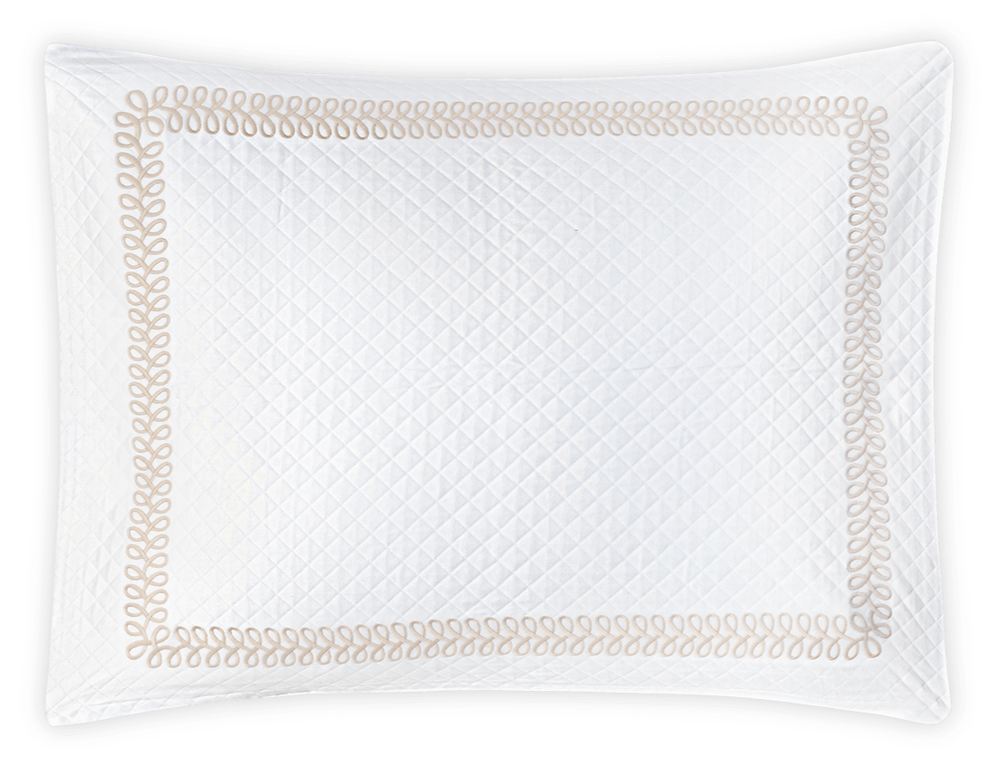 White rectangular pillow featuring a quilted diamond pattern inspired by the Astor Braid Matelassé Bedding Collection, Dune, by Matouk, with a decorative beige braided edge against a black background.
