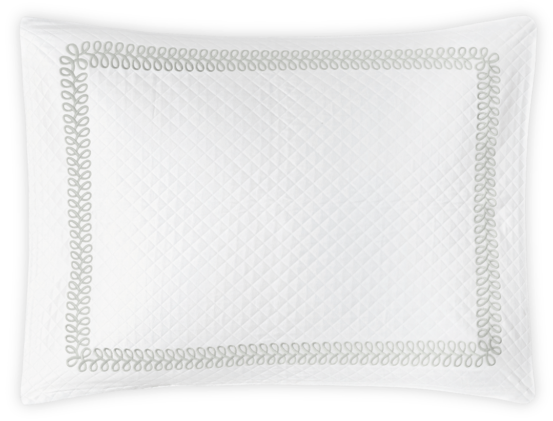 The Matouk Astor Braid Matelassé Bedding Collection in Silver features a white quilted pillow sham with a Petra diamond pattern and an elegant gray Astor Braid embroidery border.