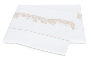 Two folded white pillowcases from the Matouk Atoll Bedding Collection, Dune, crafted from 520-thread count Ceylon cotton percale, feature an elegant beige embroidered edge pattern and are displayed on a plain background.