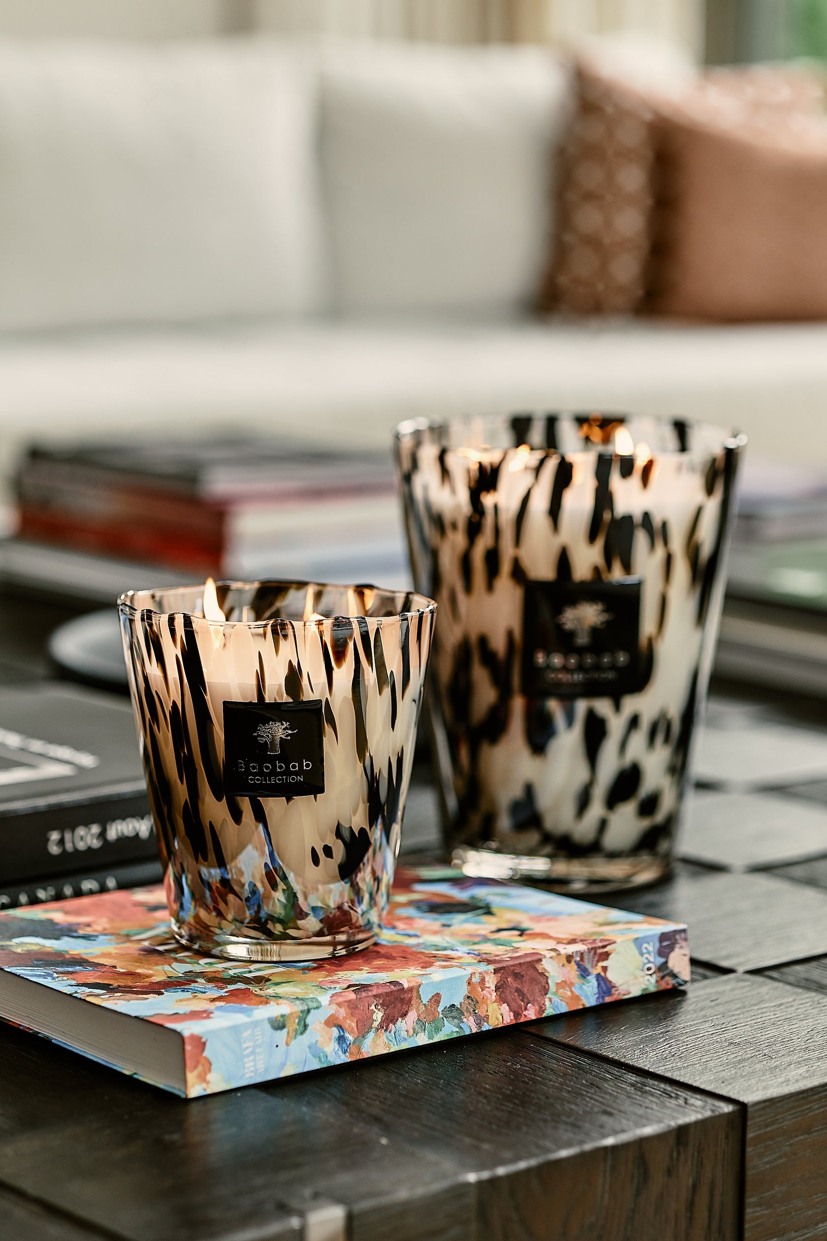 Two decorative Baobab Collection Pearls Black Candles with leopard print designs placed on a coffee table with books are enhanced by the Ginger Grapefruit Rose scent.