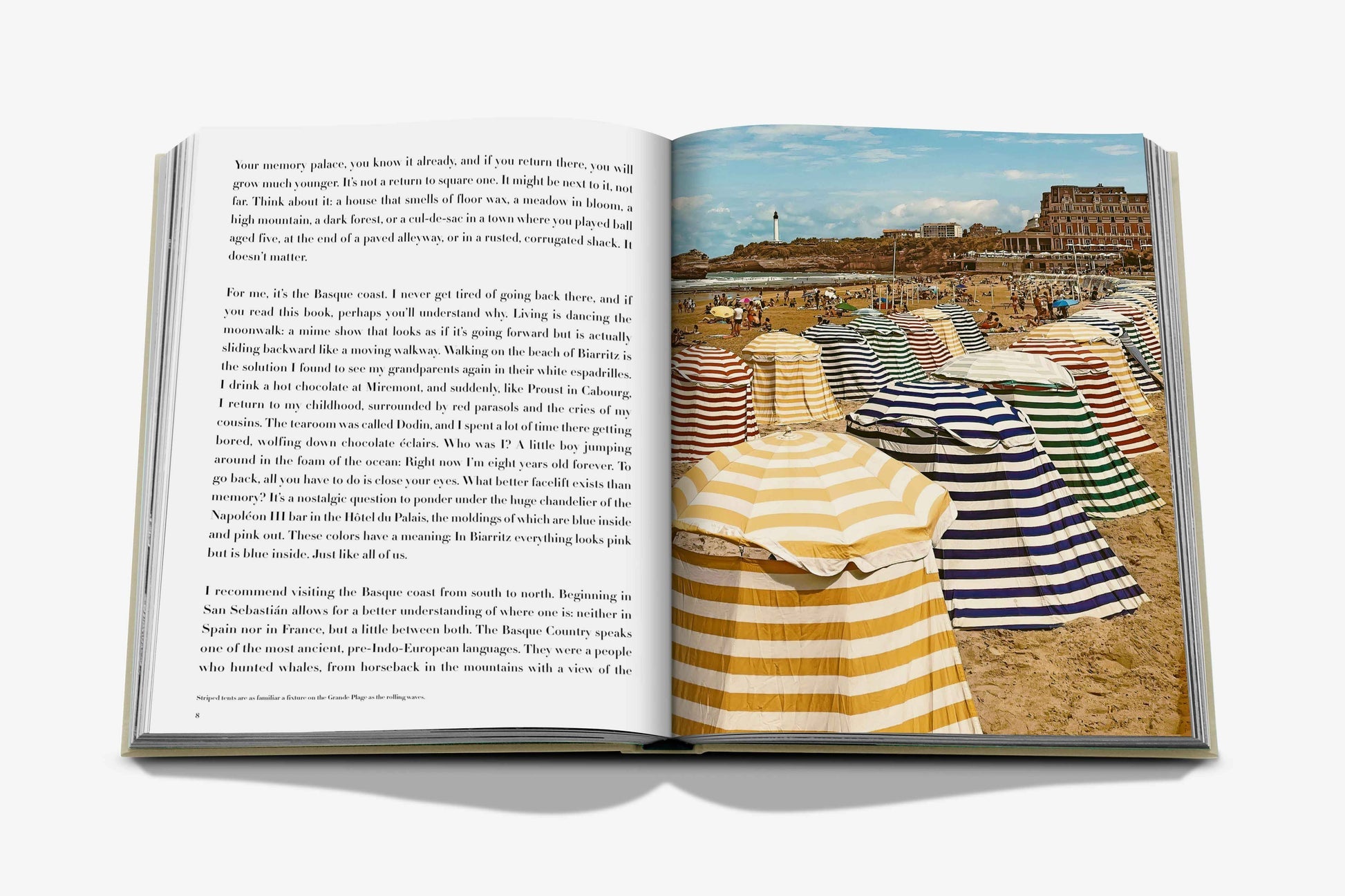 Open book displaying a page of text on the left and a color photograph of a beach in Biarritz with striped tents and buildings in the background on the right, capturing the vibrant essence of the Basque Country, from "Biarritz Basque" by Assouline.