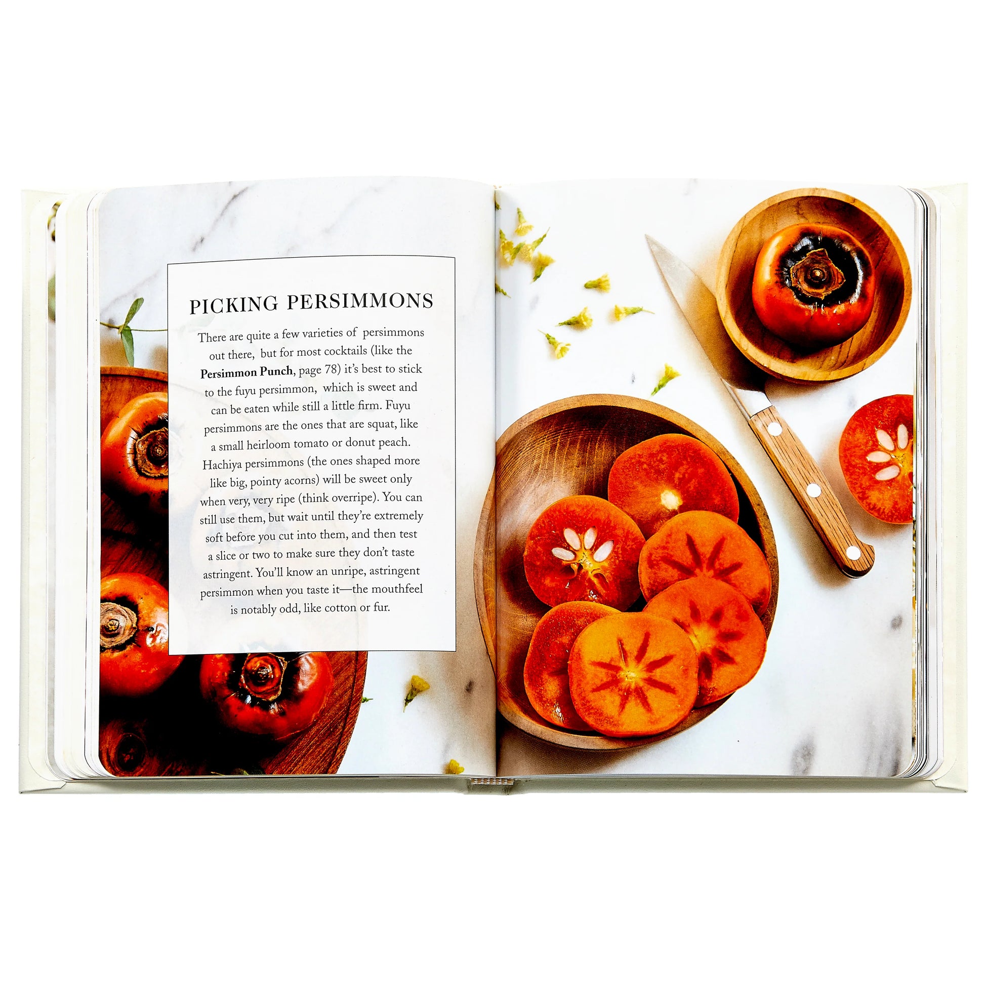 An open Graphic Image Bubbly cookbook displays a "Picking Persimmons" section with whole and sliced persimmons plus a knife on a white surface—great inspiration for festive drinks or brunch cocktails.