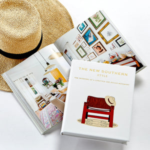 A straw hat, an open interior design book, and Graphic Image’s "The New Southern Style" are arranged on a white surface, highlighting Southern interior design.