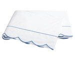 A folded white bedsheet from the Matouk Butterfield Bedding Collection, Ocean, featuring blue scallop detail and a thin blue line, shown on a plain background.