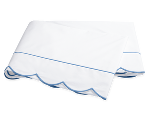 A folded white bedsheet from the Matouk Butterfield Bedding Collection, Ocean, featuring blue scallop detail and a thin blue line, shown on a plain background.