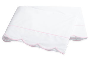Two folded white pillowcases from the Matouk Butterfield Bedding Collection, featuring light pink piped edges and scallop detail, crafted from Egyptian cotton percale.