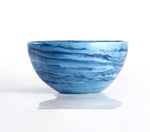A round ceramic bowl with blue and white marbled patterns, displayed on a reflective white surface—perfect as shatter-resistant decor or paired with the Denim Resin Serveware Collection from Nashi Home for a stylish touch.