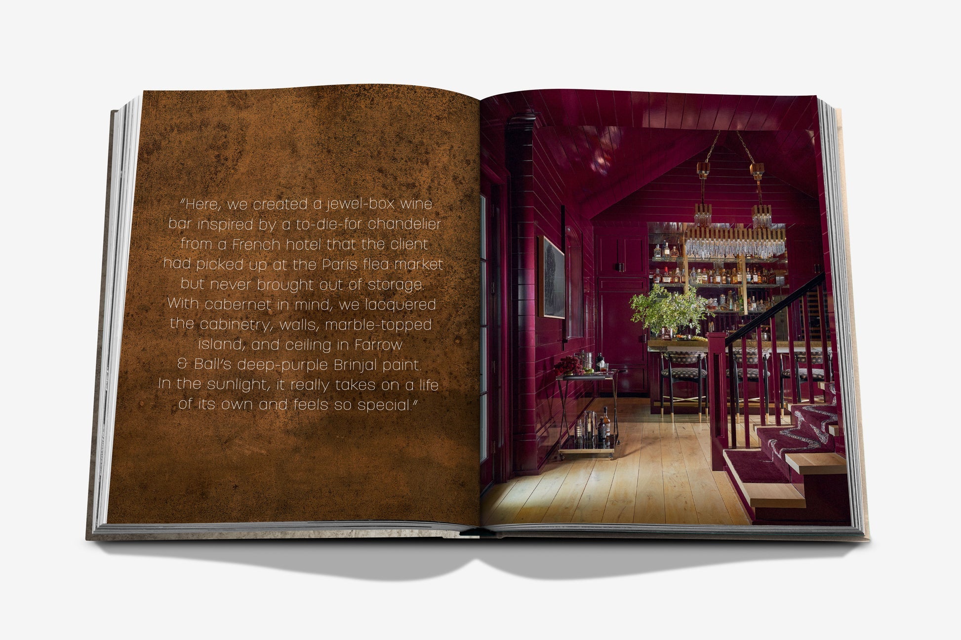 An open book titled "Relaxed Luxury" by Assouline features a quote on the left page and a photo of a Chad Dorsey-designed, red-toned home bar with chandeliers and wooden floors on the right.