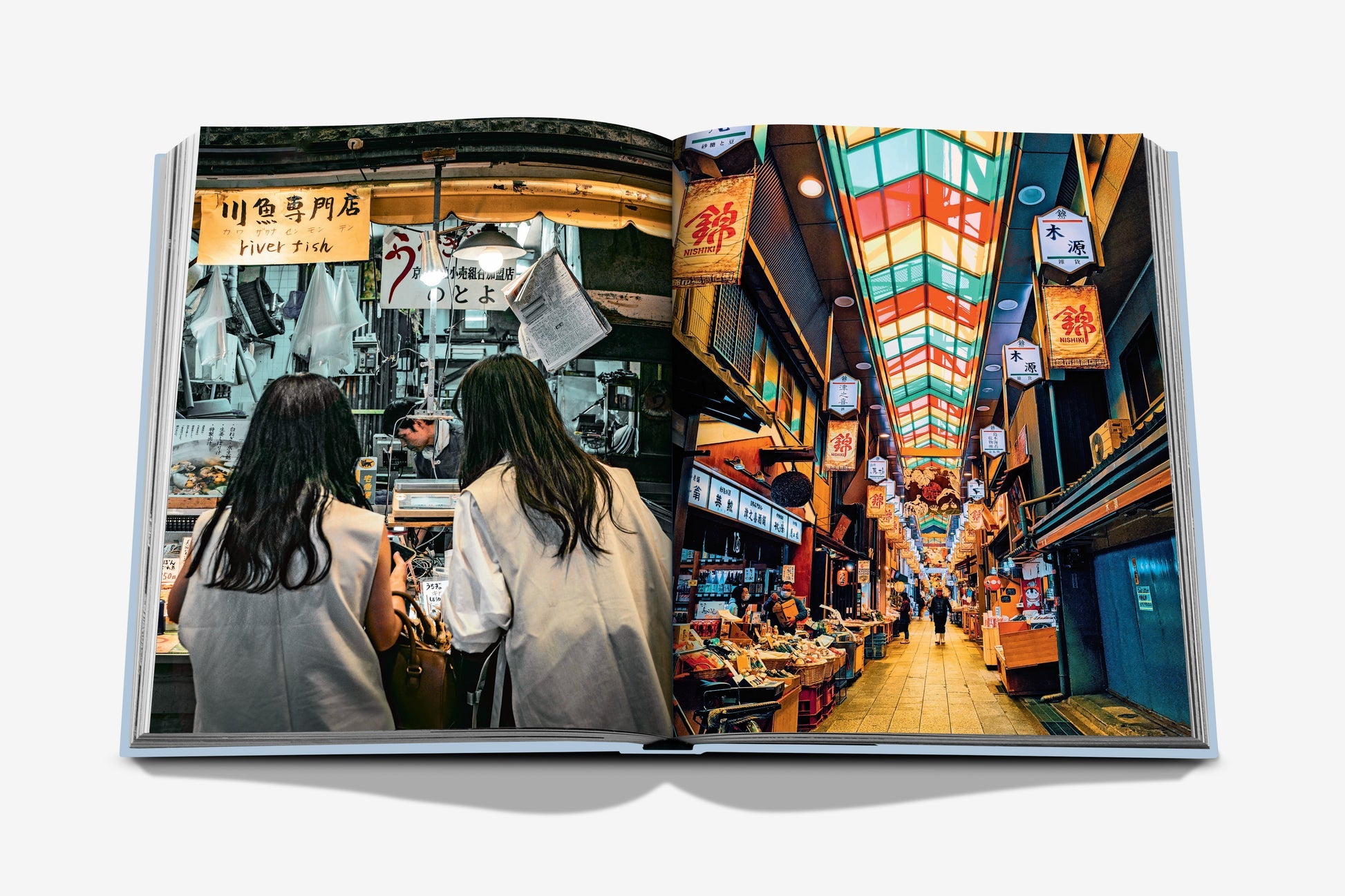 An open book by Assouline showcases two women exploring a vibrant street market, embodying Japanese culture. Among colorful signs and diverse products, the scene contrasts Kyoto Serenity with the lively spirit of Gion Matsuri.