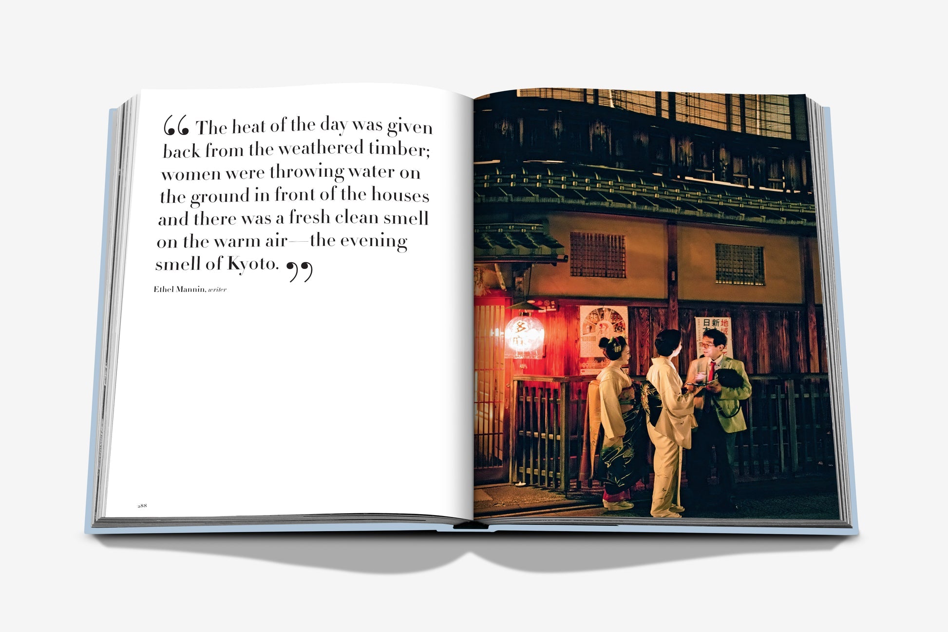 An open book from Assouline's "Kyoto Serenity" shows a left page of text and a right page photo of three people in front of a traditional building at night, capturing the essence of Japanese culture.
